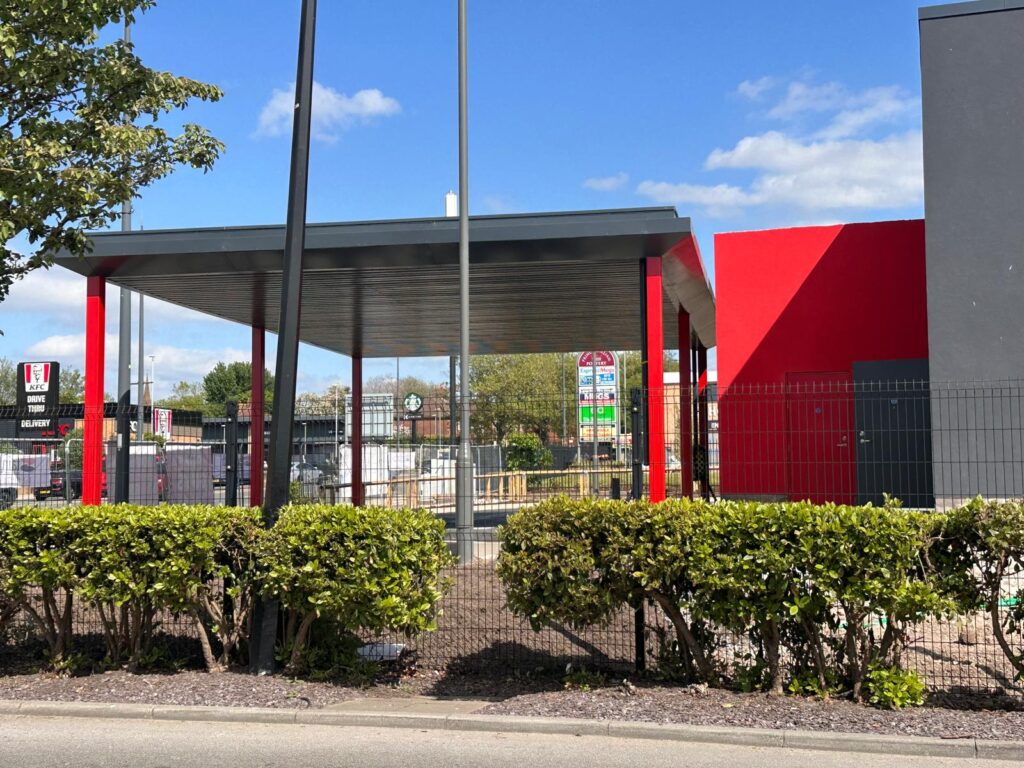 Exterior view of the new Five Guys drive-thru under construction at Liverpool Shopping Park, with bold red and grey design and nearby signage for KFC and Starbucks.